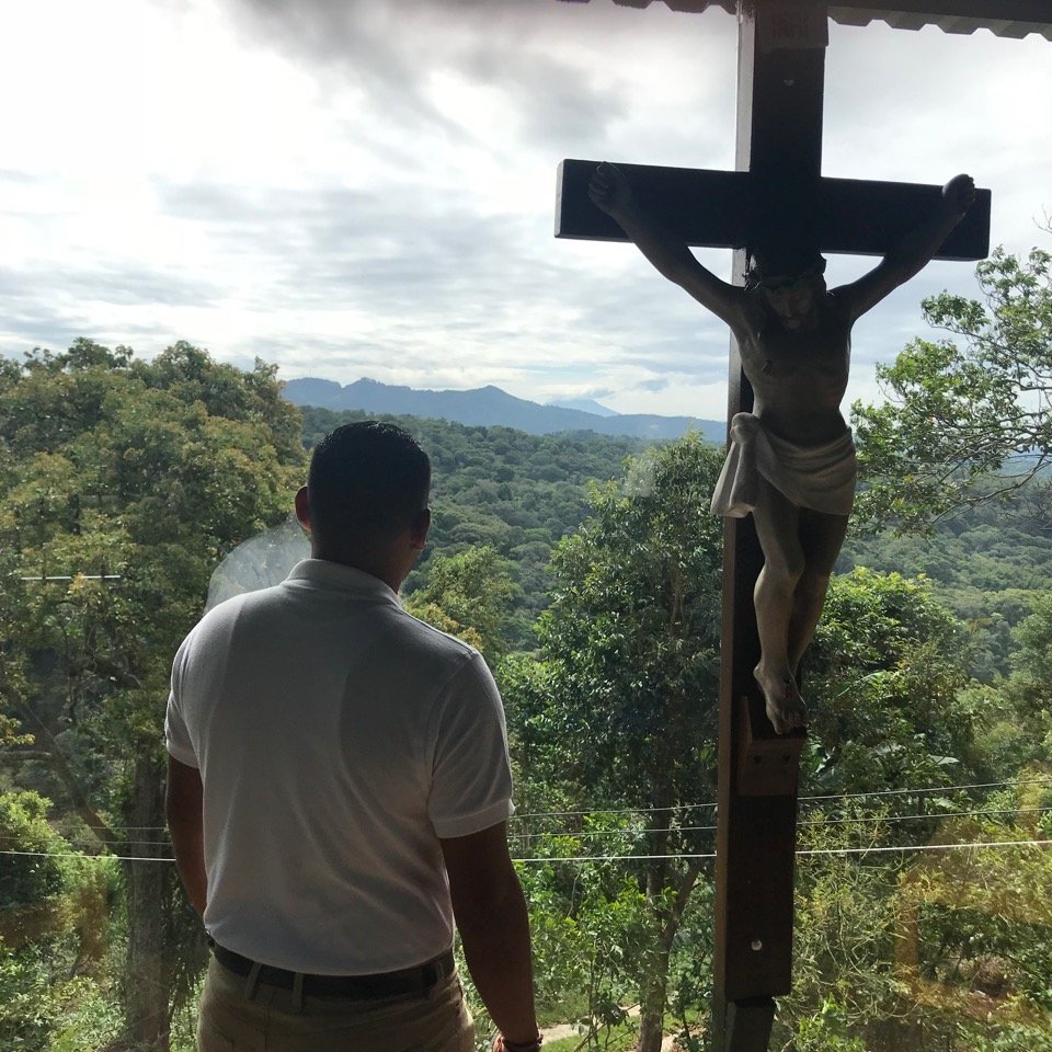 Man by crucifix, gazing out window at countryside